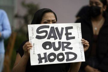 A tenant holds a sign reading “Save Our Hood,” at a community rally in the Baldwin Hills neighborhood urging Boston University officials not to sell their buildings to investors in Los Angeles, Monday, Dec. 26, 2022. (Photo by Damian Dovarganes / AP Photo)
